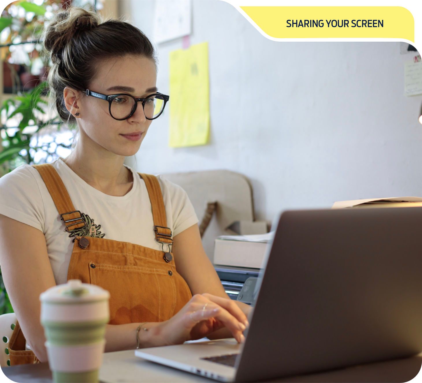 A woman using a laptop in a bright room with plants